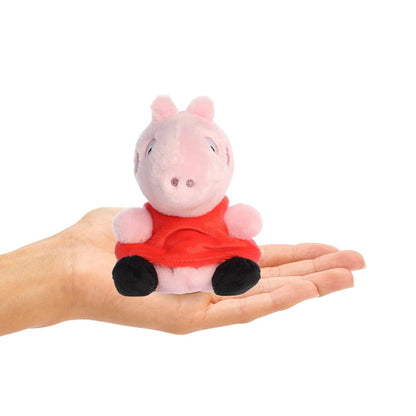 Small pink plush toy with a red shirt held in a hand on a white background