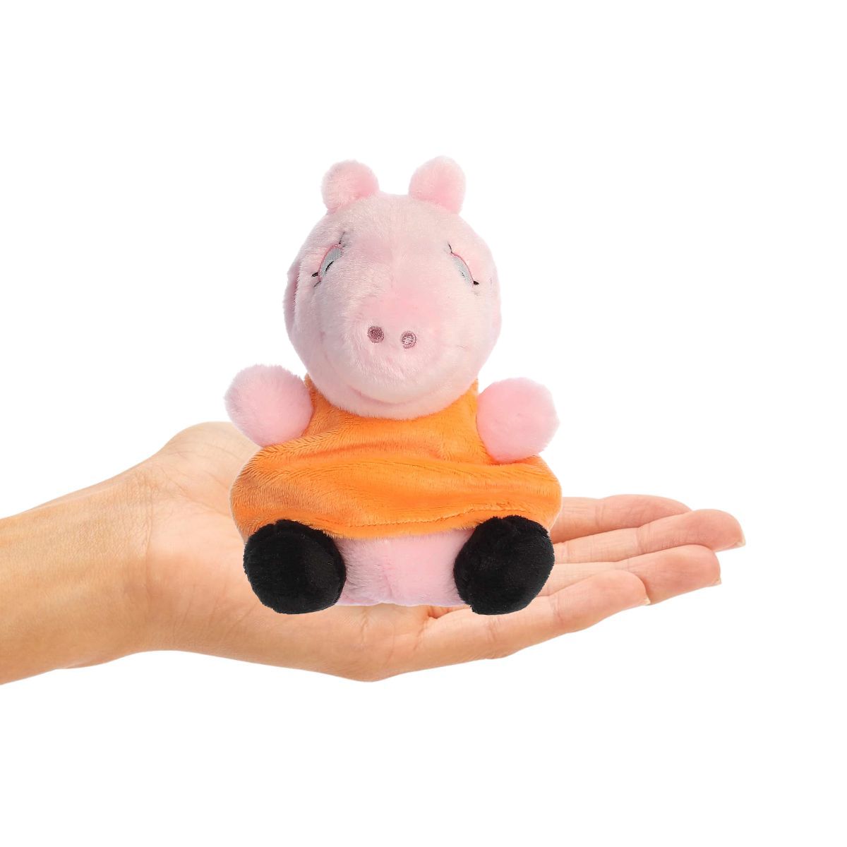 Plush toy of a pink pig character with an orange dress held in a hand on a white background