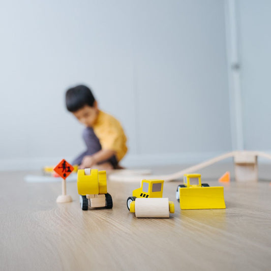 A happy child engaging in imaginative pretend play with a PlanToys wooden vehicle toy.