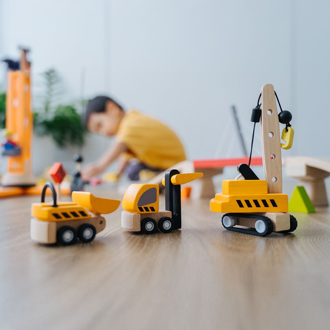 A toddler practicing hand-eye coordination by arranging the PlanToys eco-friendly construction trucks on the floor.