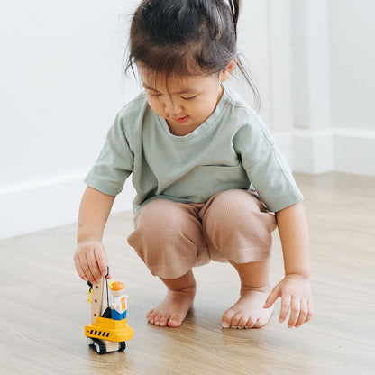 A young child holding the non-toxic PlanToys wooden construction vehicle during focused playtime.