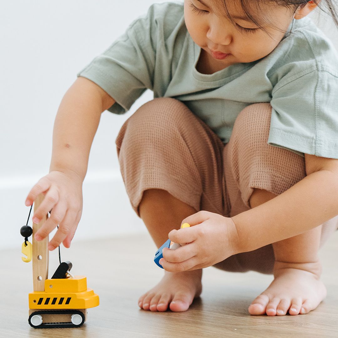 A toddler interacting with the movable parts of the durable PlanToys wooden crane truck.