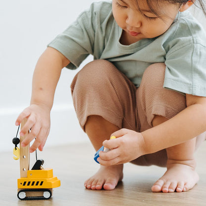 A toddler interacting with the movable parts of the durable PlanToys wooden crane truck.