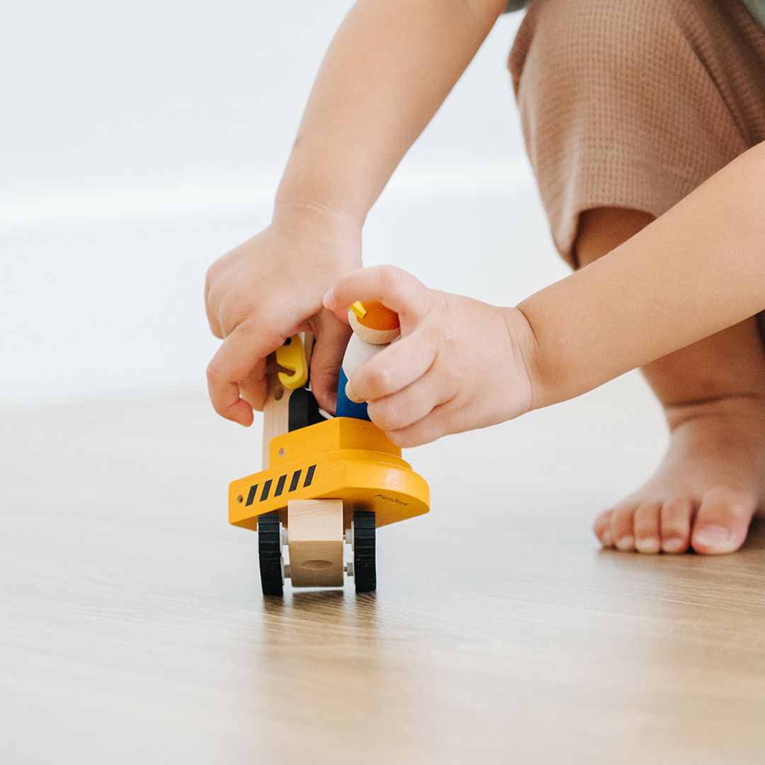 Close-up of a child's hands operating the movable forks on the PlanToys wooden forklift toy.