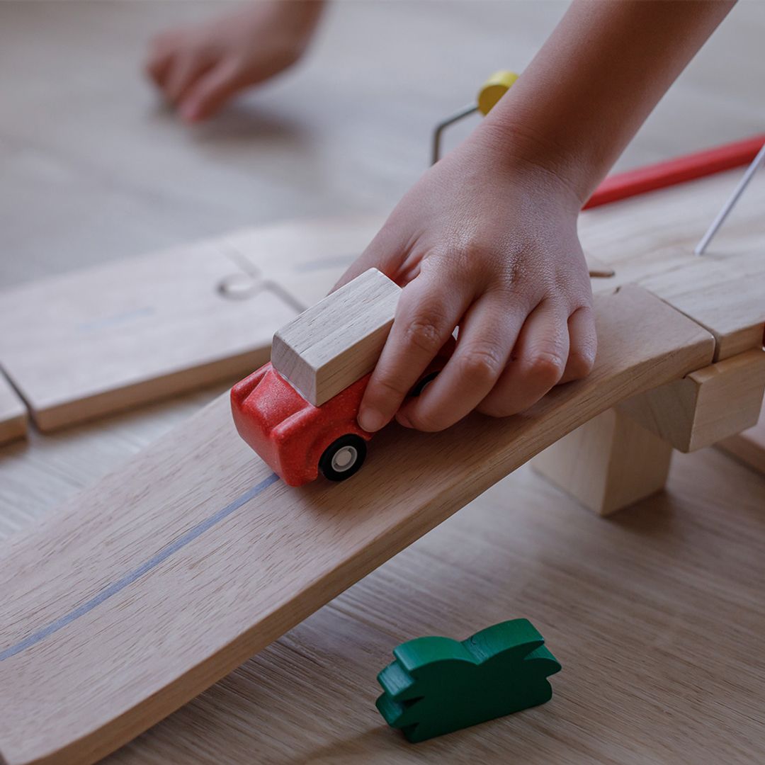 Lifestyle shot showing a toy car driving smoothly along the non-toxic PlanToys wooden road system.