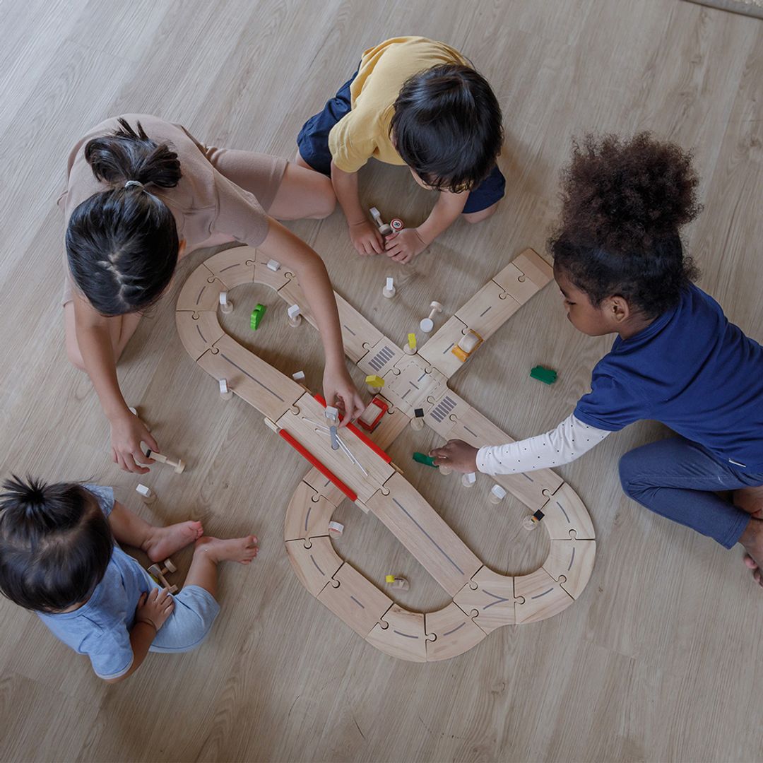 Four children engaging in collaborative, imaginative play while building a massive PlanToys eco-friendly track layout.