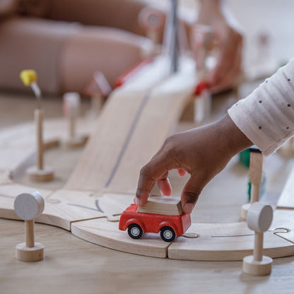 A toddler developing fine motor skills and spatial awareness by piecing together the earth-friendly PlanToys road set.