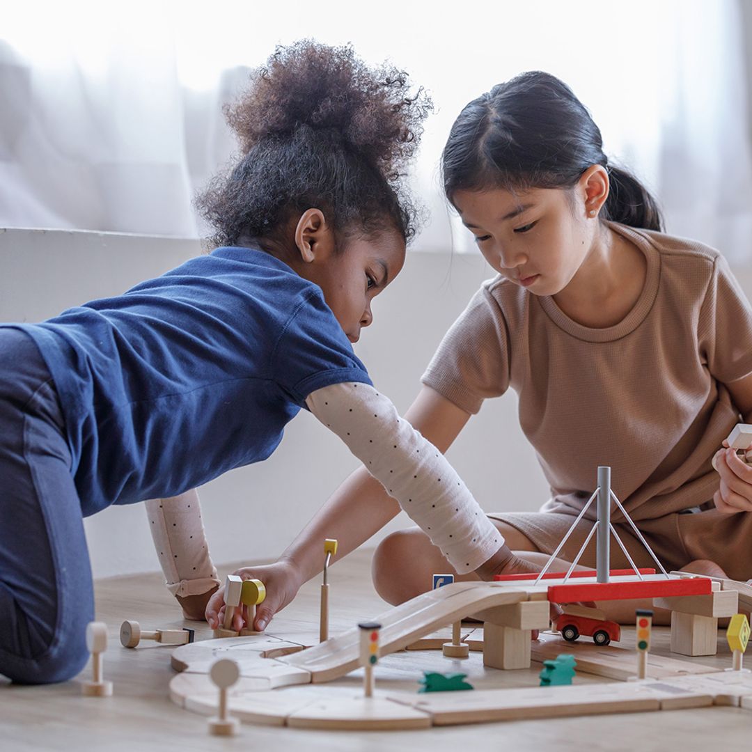Two kids working together to design a custom street layout using the versatile PlanToys wooden road system.