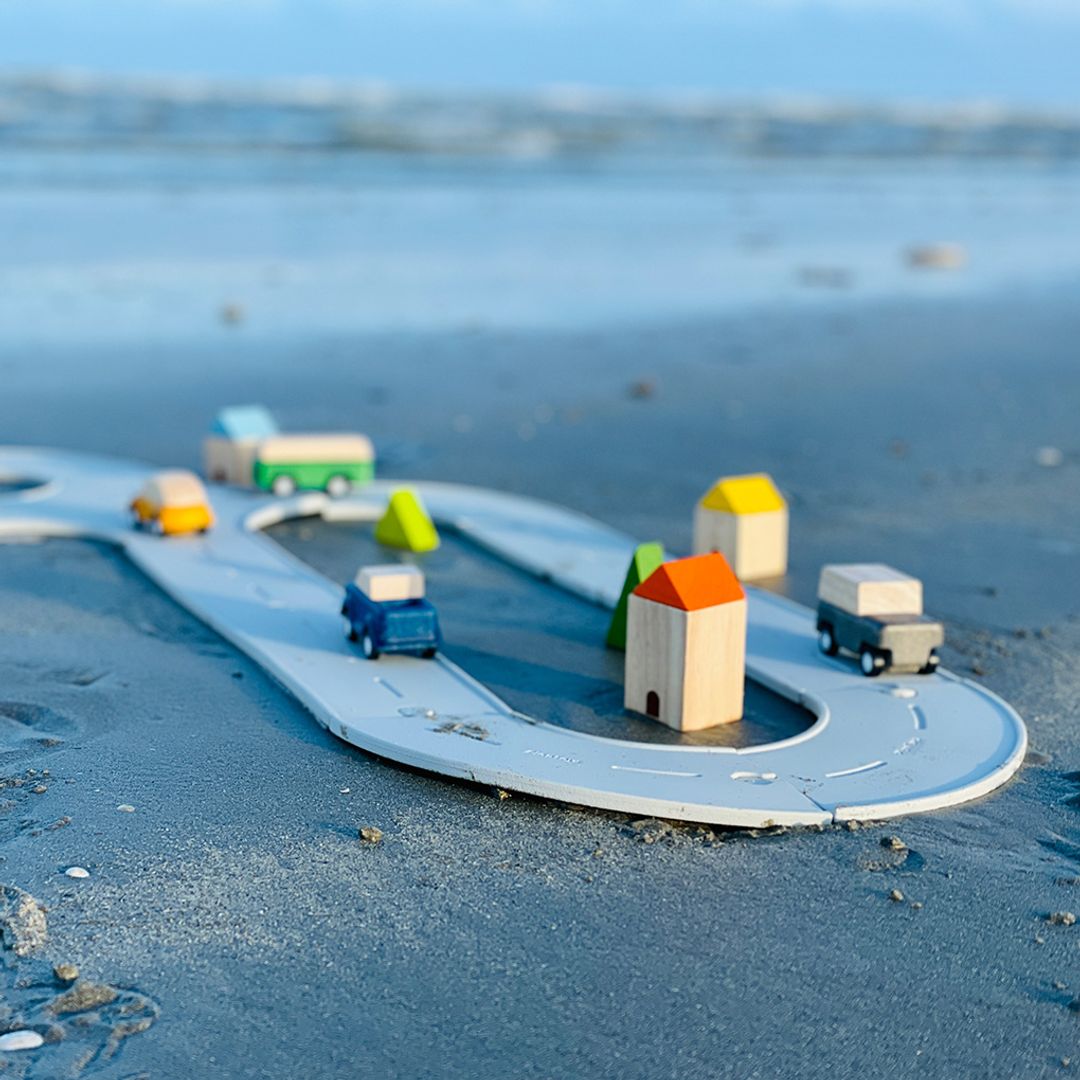 The versatile PlanToys flexible rubber road and rail set being used for sensory play on a wet sandy beach.