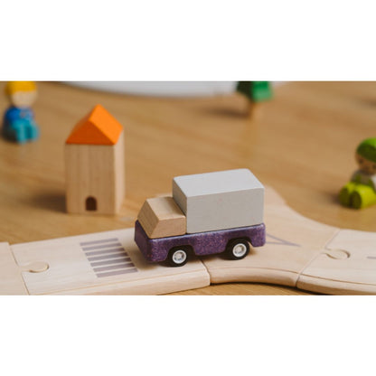 PlanToys wooden purple delivery truck toy on a wooden track with small figures and a house in the background