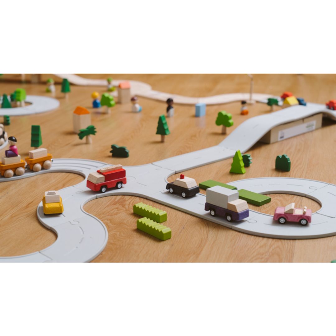 PlanToys wooden purple delivery truck toy set in a layout with roads, cars, and trees on a wooden surface