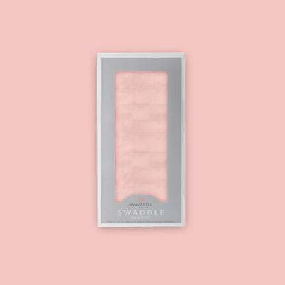 Straight front view of the packaged Newcastle Classics Pink Rose bamboo muslin swaddle blanket in a grey window box set against a matching solid pink background.