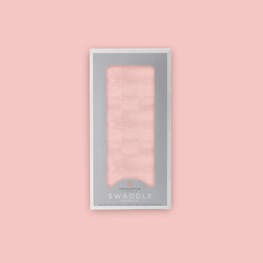 Straight front view of the packaged Newcastle Classics Pink Rose bamboo muslin swaddle blanket in a grey window box set against a matching solid pink background.
