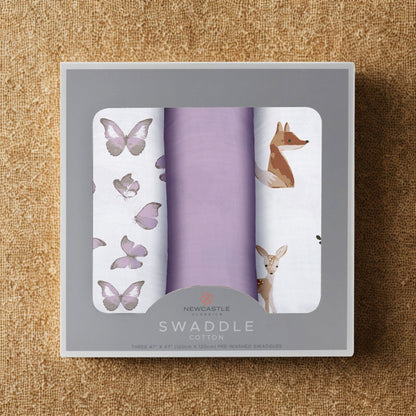 Straight top-down view of the packaged Mountain Meadow baby swaddle blankets inside a grey Newcastle Classics 3-pack box resting on a textured cork surface.