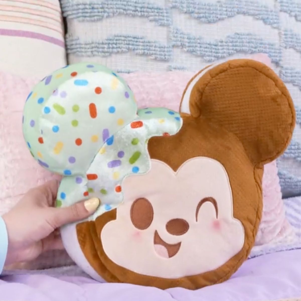 Lifestyle image showing a person's hands gently squeezing the ultra-squishy 10-inch Disney Munchlings Squeeze-A-Munch Mickey Mouse plush.