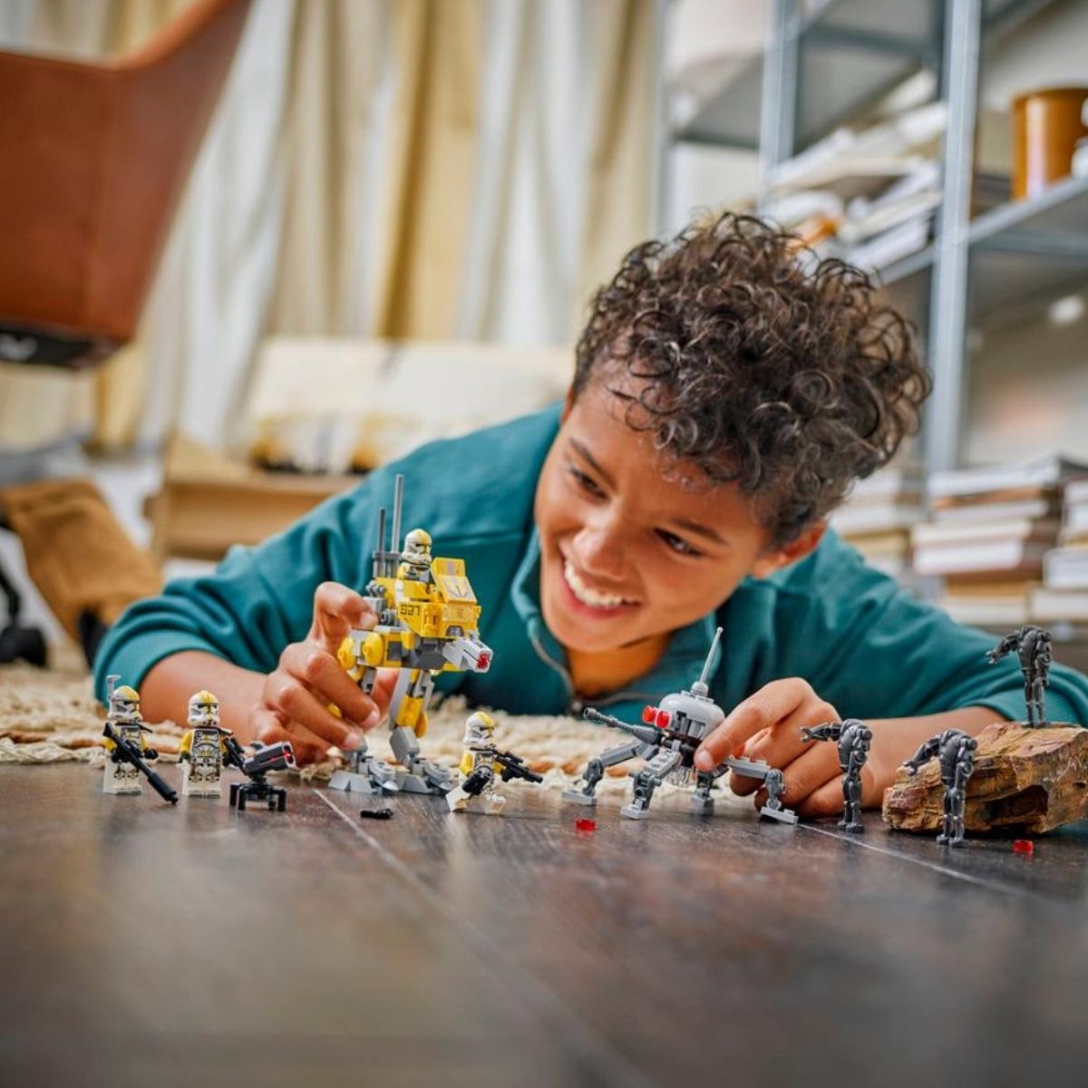 A young child smiling on the floor while posing and playing with the completed LEGO® Star Wars Clone Trooper figures and walkers.