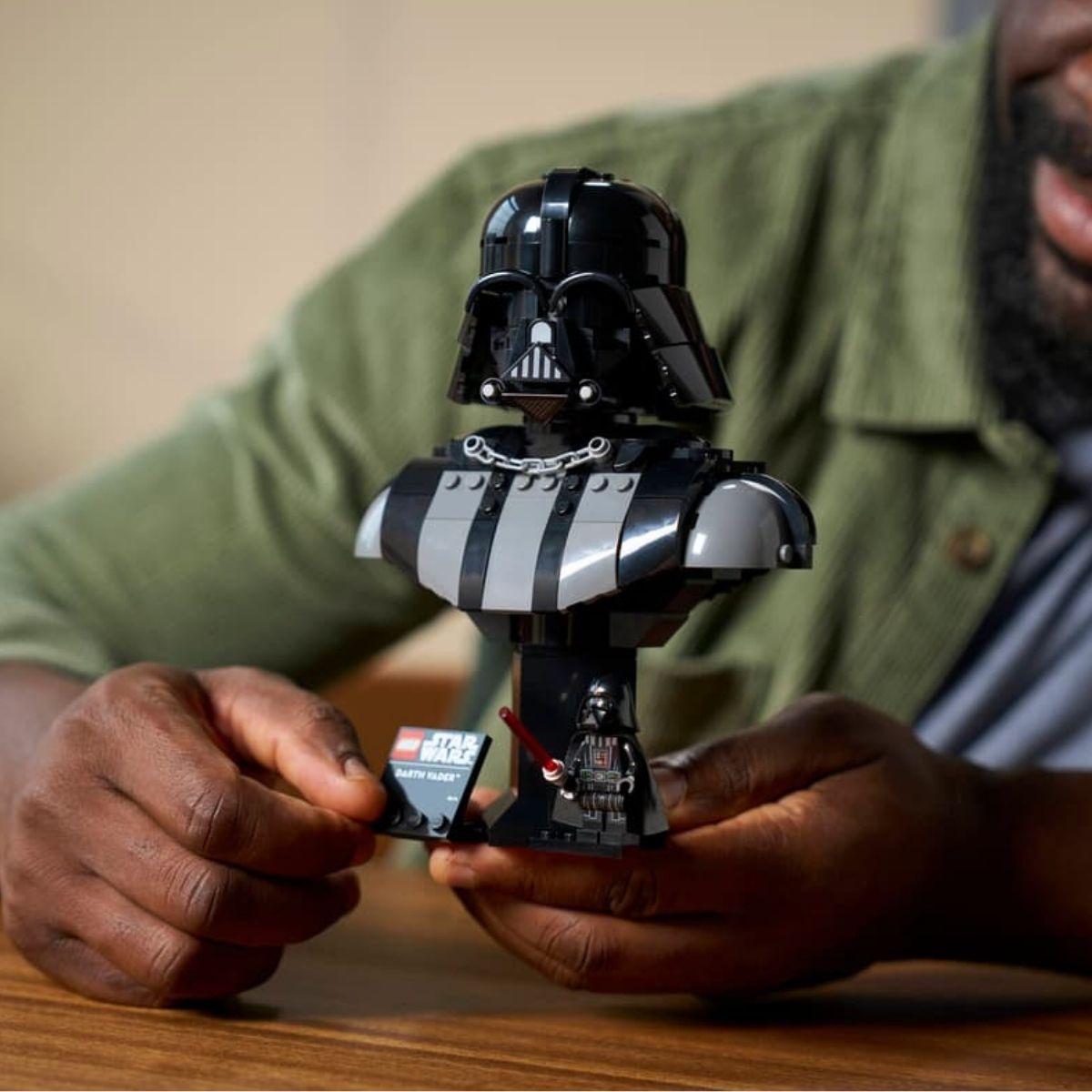 A person's hands adjusting the completed 349-piece LEGO® Star Wars Darth Vader bust model on a wooden table.