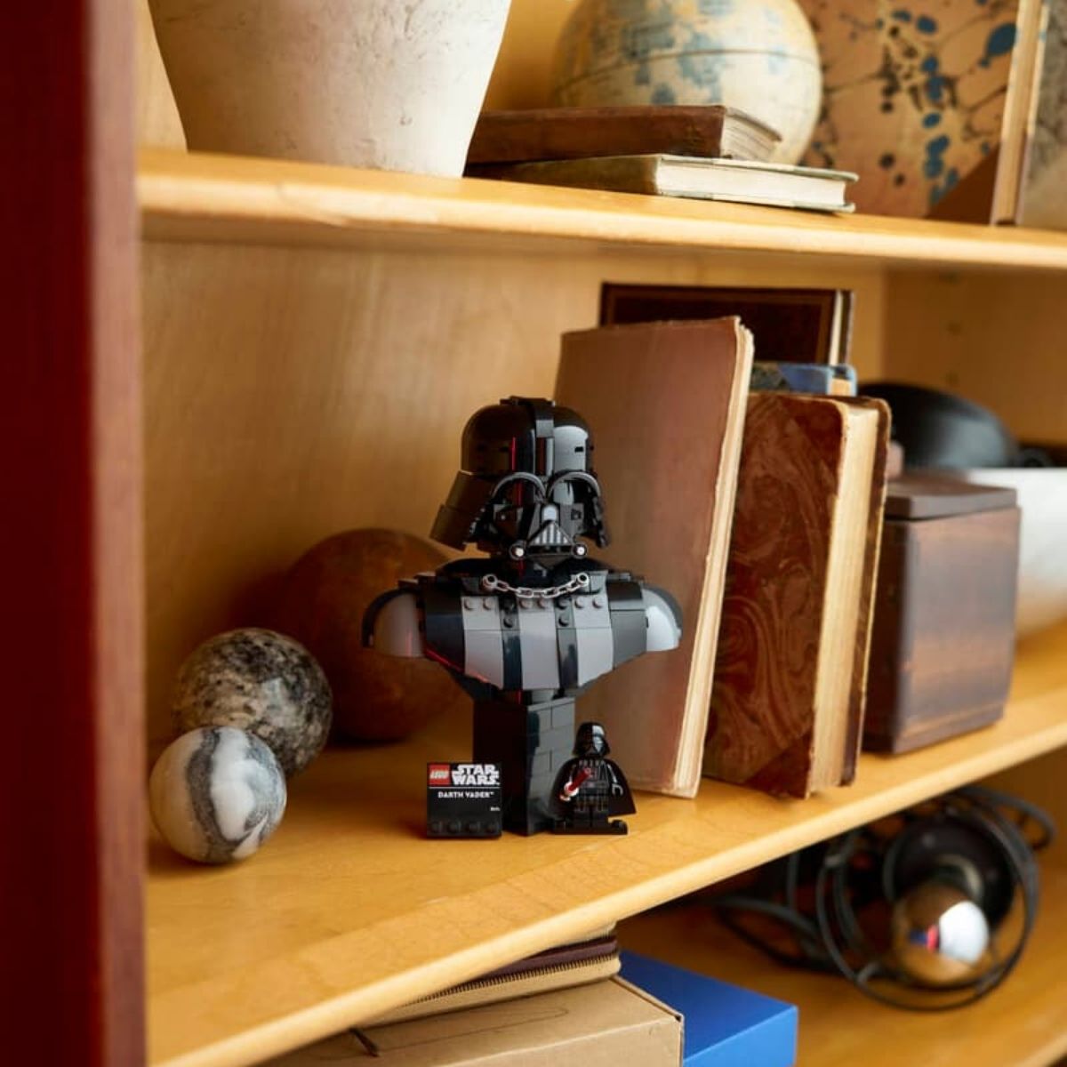 The assembled LEGO® Star Wars Darth Vader bust showcased on a wooden bookshelf next to decorative items.