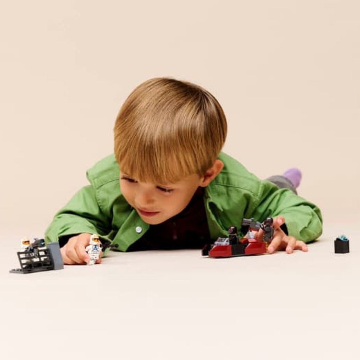 A young boy laying on the floor playing with the vehicles and minifigures from the LEGO® Star Wars Mandalore battle pack.