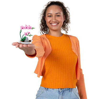 A smiling woman presenting a completed miniature pink orchid replica in her hand to showcase its small scale.