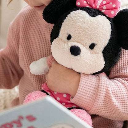 Lifestyle image showing a child happily hugging the soft 12-inch Disney Baby Cuteeze Minnie Mouse stuffed animal while reading a book.