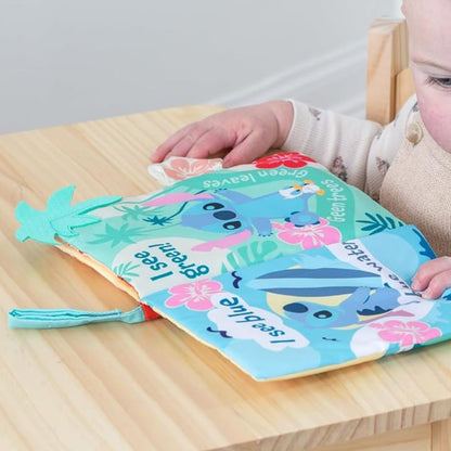 A baby sitting at a low wooden table turning the pages of the colorful soft blue and green Stitch activity book.