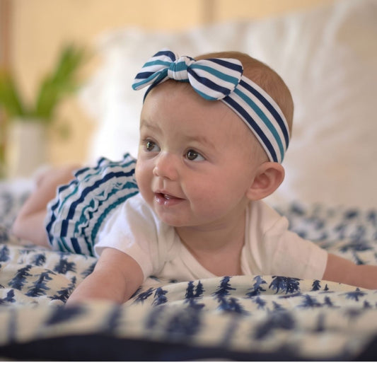 Baby girl wearing the Newcastle Classics Ultimate Road Trip blue striped headband and matching ruffled bloomers playing on a blanket.