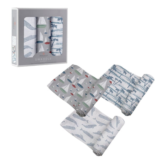 Three Newcastle Classics Ocean Tides bamboo muslin swaddle blankets partially unrolled next to their grey 3-pack window packaging box.