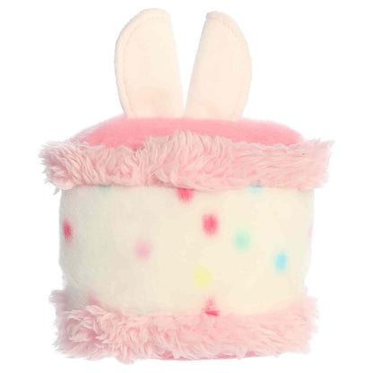 Back view of the Aurora Palm Pals cake plush toy showing its colorful speckled back, pink frosting edges, and the back of its bunny ears.