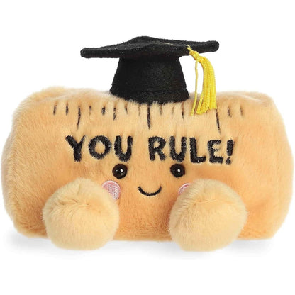 Front view of the 5-inch Aurora Palm Pals You Rule ruler plush toy wearing a black graduation cap and featuring a smiling face.