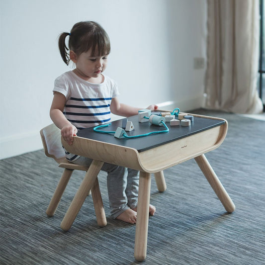 A young girl playing with toys on the sturdy, eco-friendly PlanToys black children's activity table.