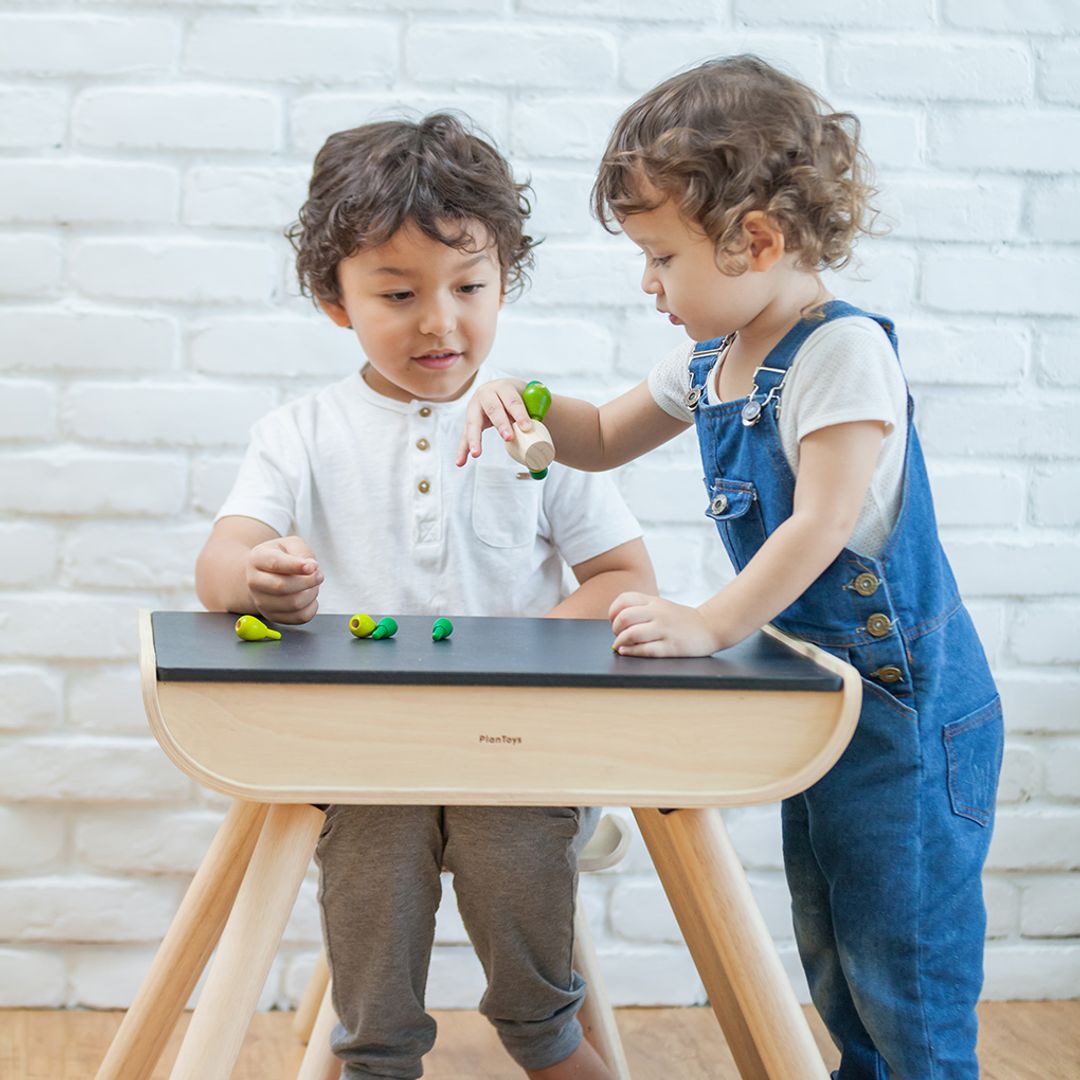 Two toddlers engaging in collaborative play while standing at the sustainable PlanToys wooden activity table.