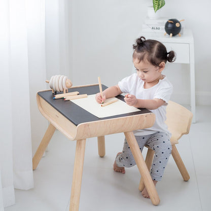 Lifestyle shot of a child doing arts and crafts at the earth-friendly PlanToys toddler desk and chair set.