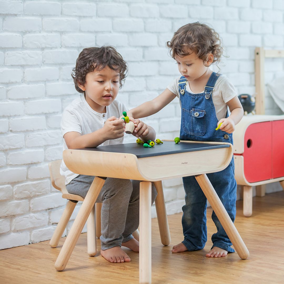 Siblings enjoying screen-free playtime together around the non-toxic PlanToys wooden table and chair set.
