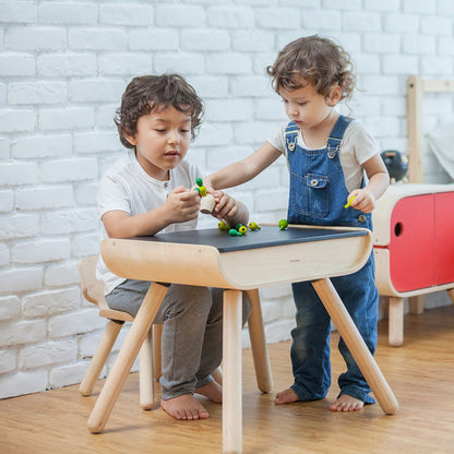 Siblings enjoying screen-free playtime together around the non-toxic PlanToys wooden table and chair set.