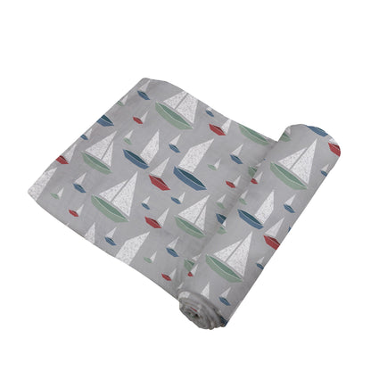 Angled view of the grey swaddle blanket with colorful sailboats partially unrolled to show its soft texture.