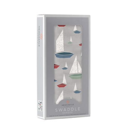 Angled front view of the packaged Marina Sailboats baby swaddle blanket folded inside a light grey Newcastle Classics window display box.