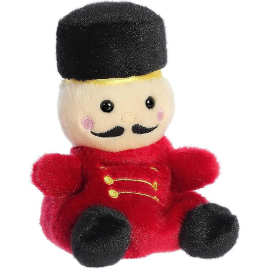 Aurora 5-inch Palm Pals Marius Nutcracker plush toy sitting at an angle showing its red uniform coat with gold stitching, tall black hat, and prominent black handlebar mustache.
