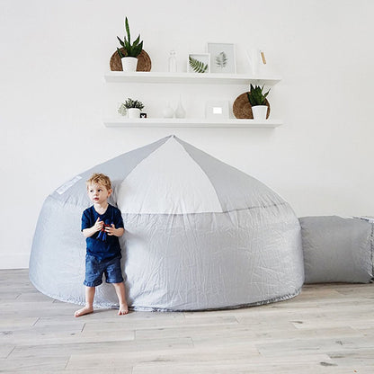 A young boy standing proudly next to the inflated Mod About Gray AirFort in a minimalist, modern living room.