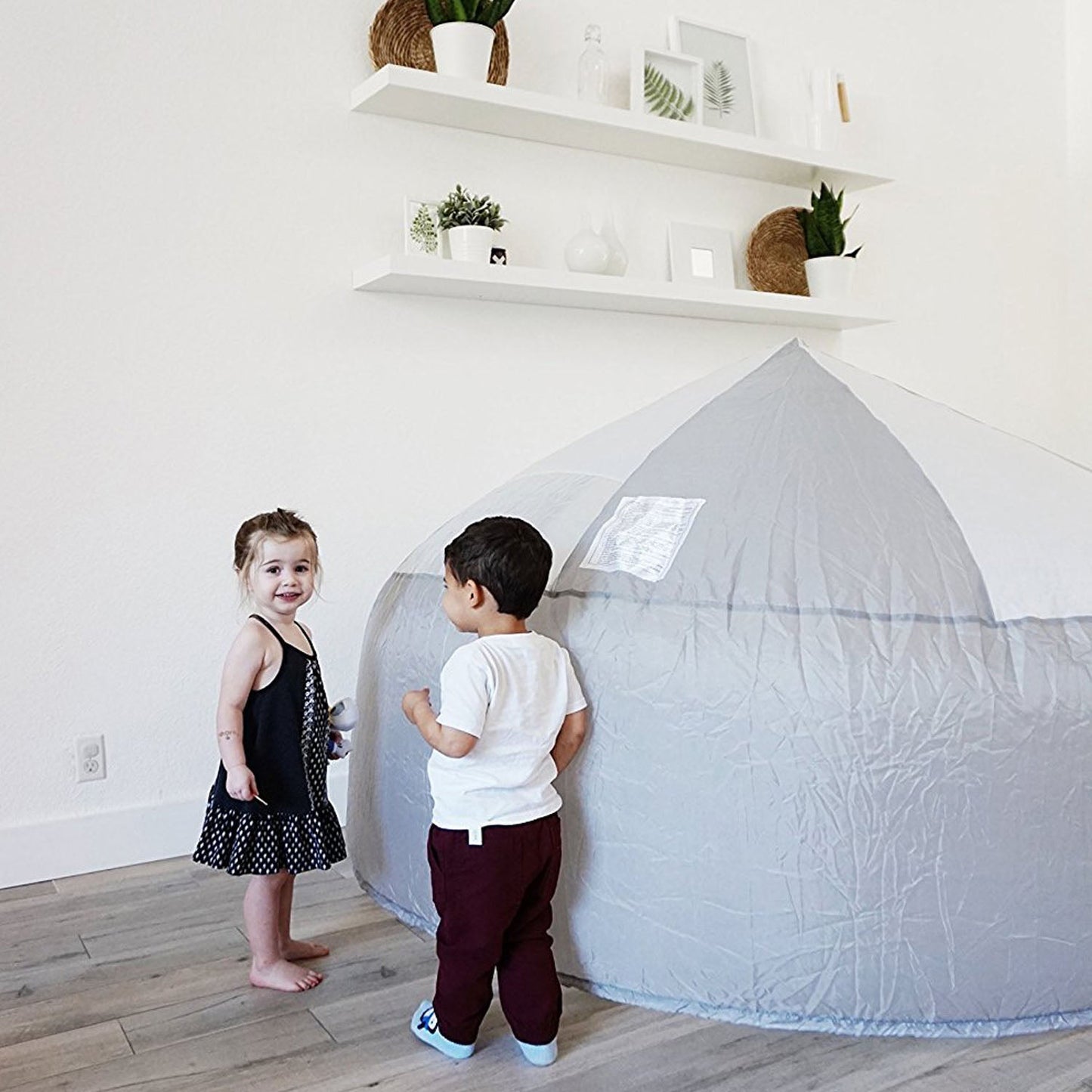 Two young children standing together next to the Mod About Gray AirFort in a modern home.