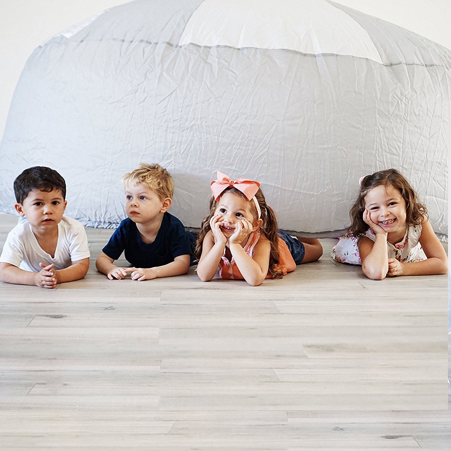Four children lying on their stomachs, smiling and looking out from under the hovering edge of the spacious gray AirFort.