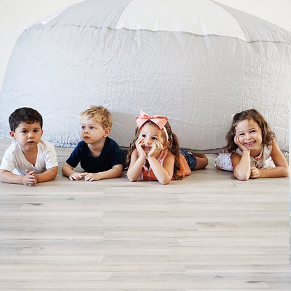 Four children lying on their stomachs, smiling and looking out from under the hovering edge of the spacious gray AirFort.