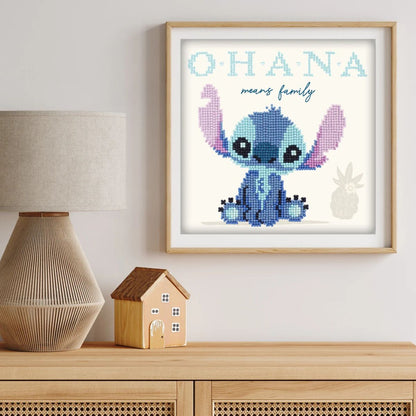 Completed Stitch diamond painting displayed in a light wood frame sitting on a wooden console table next to a lamp.