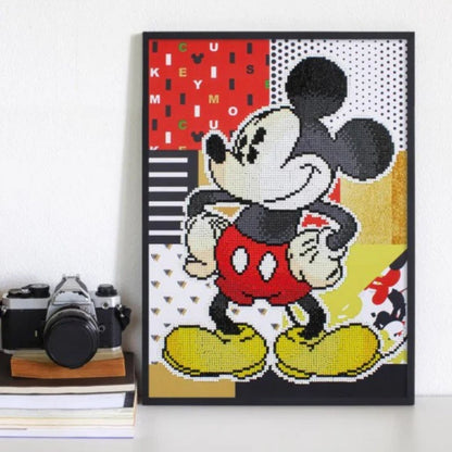 Completed Retro Mickey diamond painting displayed in a black frame sitting on a white desk next to books and a vintage camera.