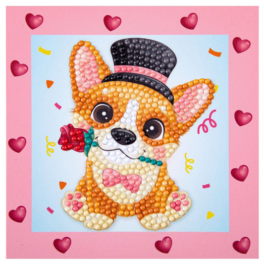 Finished DIAMOND DOTZ Corgi Top Hat diamond painting featuring a corgi puppy in a top hat and bowtie holding a rose with a pink heart border.