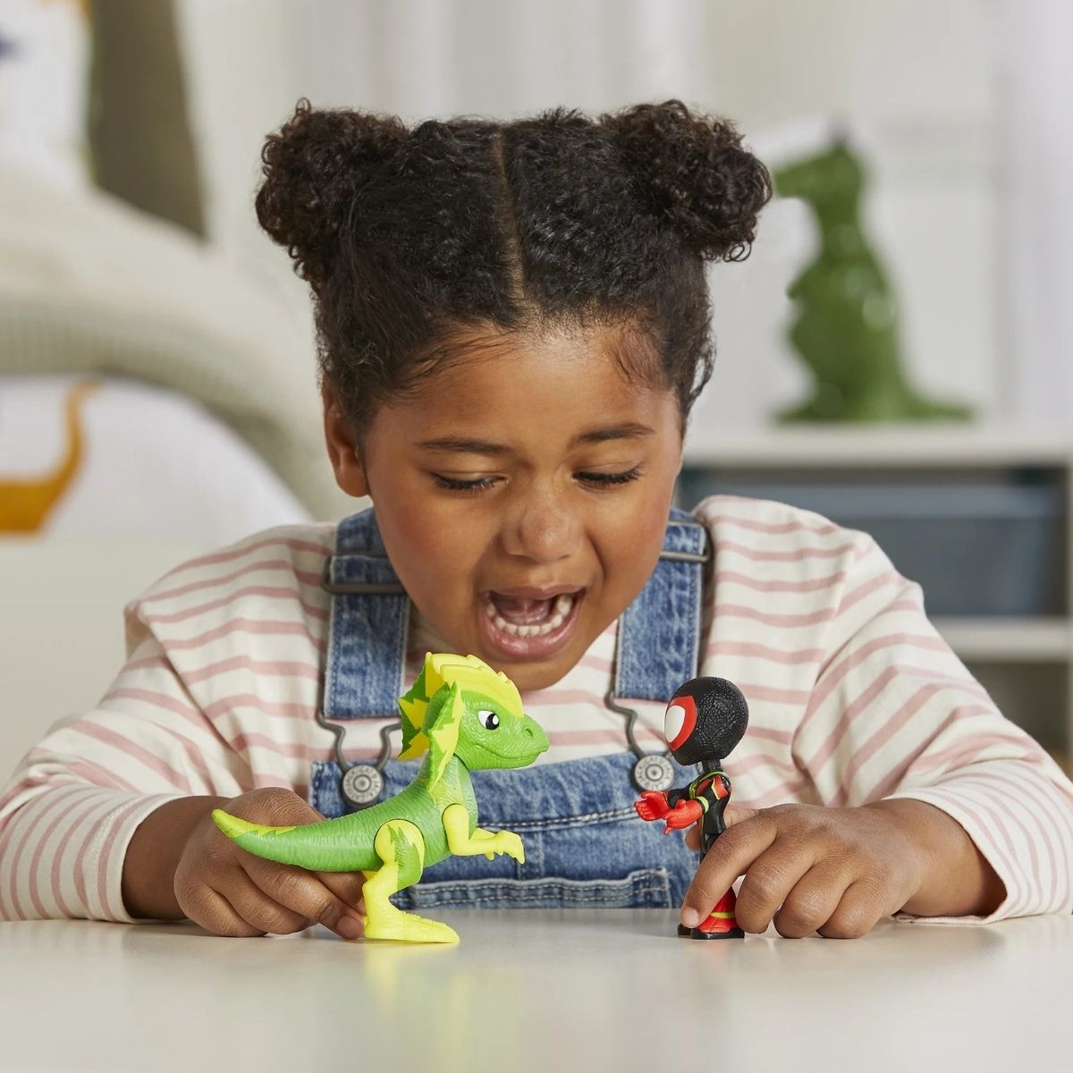 Lifestyle shot of a child making the Miles Morales and Electrosaurus toys interact on a playroom table.