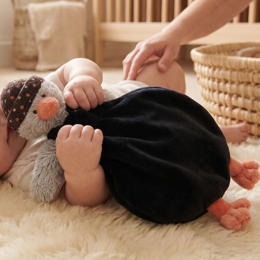 A baby cuddling the Happy Horse Penguin Polar dressed plush lovey closely while resting on a soft cream rug.