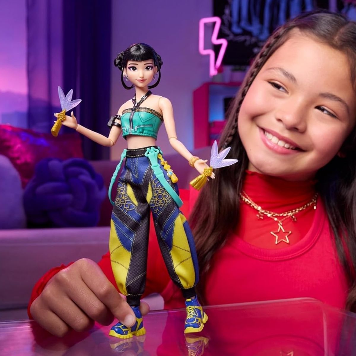 A young girl smiling while posing the articulated K-Pop Demon Hunter Zoey doll on a table during playtime.