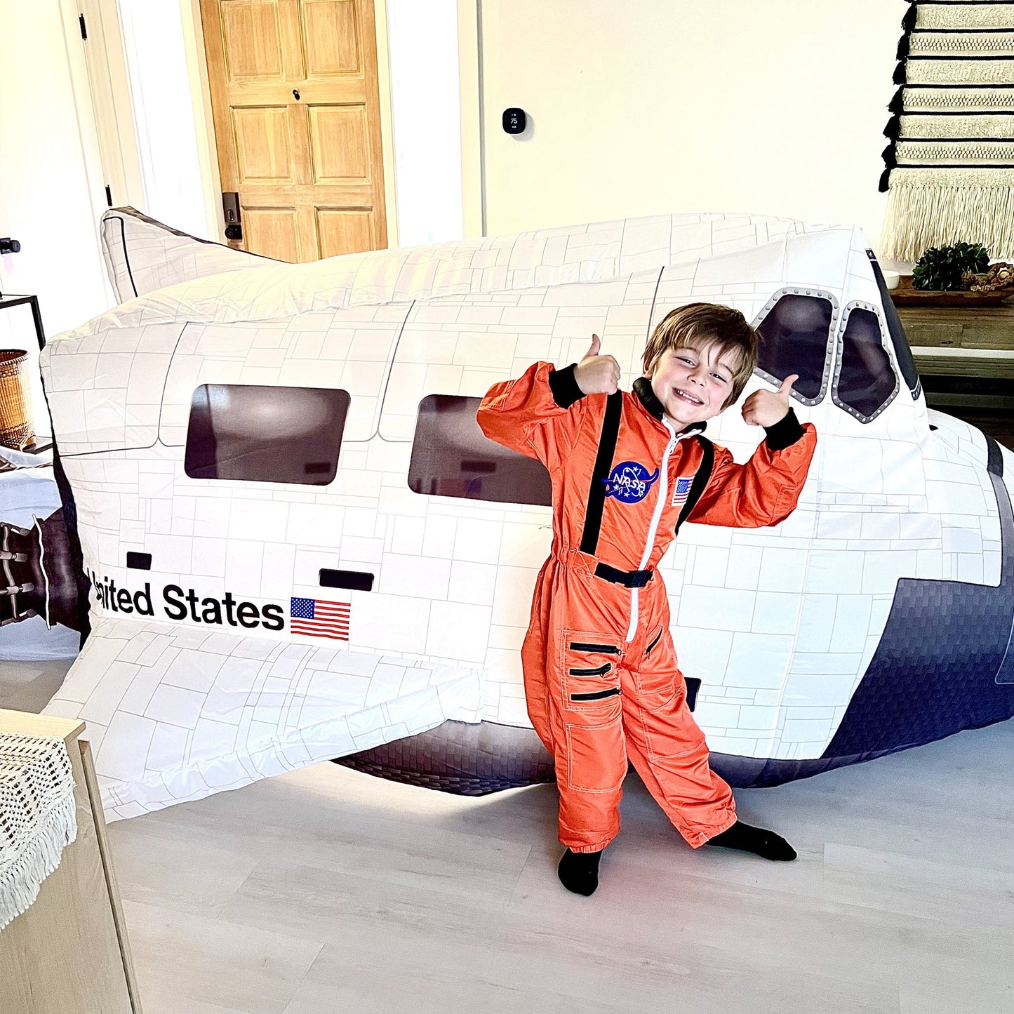 A young boy dressed in an orange astronaut suit posing excitedly next to the inflated Space Shuttle AirFort.