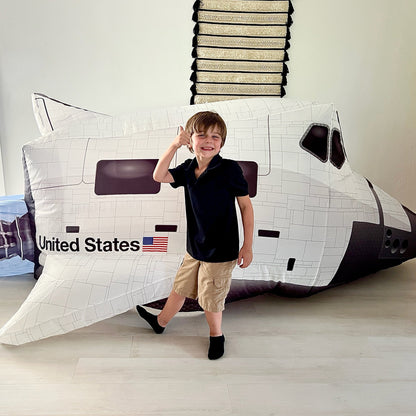 A young boy saluting playfully next to the "United States" flag graphic on the side of the inflated Space Shuttle AirFort.